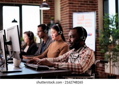 African american helpline operator with chronic impairment working at call center client care. Man wheelchair user giving telework assistance at customer service in disability friendly office.