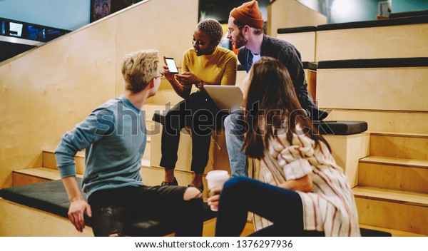 African american hipster girl showing new\
application on mobile phone to crew of colleagues, team of\
employees checking new software updates on mobile phone having\
conversation about  creative\
ideas\
