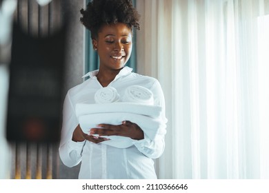 African American House Keeper At A Guest Bedroom Holding Towels While Facing Camera Smiling. Cleaning The Hotel Room. Hotel Vacations. Smiling Housekeeping Woman