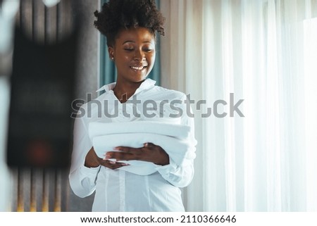 African american house keeper at a guest bedroom holding towels while facing camera smiling. Cleaning the hotel room. Hotel vacations. Smiling Housekeeping Woman