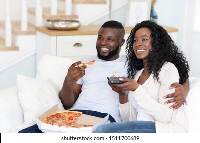 African american husband and wife eating pizza and watching TV at home, enjoying weekend together. - Powered by Shutterstock