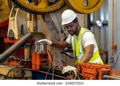 African American Industrial Worker Is Using Hydraulic Power Press Machine To Make Metal And Steel Part While Working Inside The Metal Sheet Galvanized Roof Factory For Safety Industry