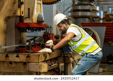 African American industrial worker is using hydraulic power press machine to make metal and steel part while working inside metal sheet galvanized roof factory for safety industry - Powered by Shutterstock