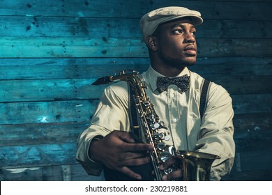 African american jazz musician with saxophone in front of old wooden wall.