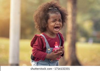 African American Kid Crying Alone On Playground At Park. Cute Afro Girl Stay Stand Alone And Show Feeling Sad With Tear On Green Park Outside Home. African American Child Emotion Concept