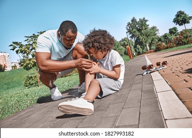 African American Kid And His Dad Looking Concerned While Inspecting A Kid Knee After A Skateboard Incident