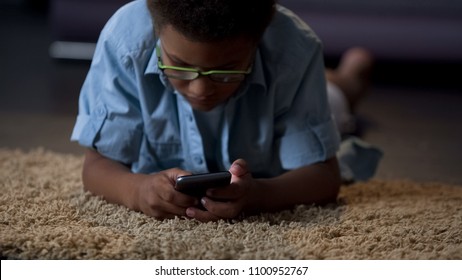 African american kid playing in application on phone comfortably lying on floor