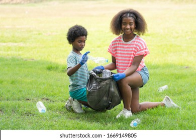 African American Kids Volunteer Picking Up Plastic Bottles Into A Black Garbage Bag At The Park, Help Garbage Collection Charity Environment