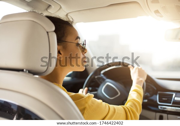 African American\
Lady Driver Driving Car Having Ride In City. Automobile Ownership.\
Back View, Selective\
Focus
