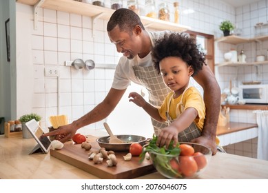 African American Little boy preparing food while his father looking on the digital recipe and using touch screen tablet in the kitchen at home. BeH3althy - Powered by Shutterstock