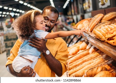 african american little child pointing by finger at pastry to father in supermarket 