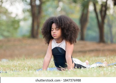 African American Little Girl Doing Meditate Yoga Asana On Roll Mat With Eyes Closed In Park. Kid Girl Practicing Doing Yoga Outdoor. Little Afro Girl With Curly Hairstyle Training Yoga