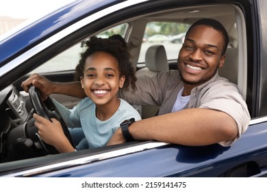 African American Little Girl Driving Car Sitting With Father In Driver's Seat Smiling To Camera. Dad Teaching His Daughter To Drive. New Automobile Purchase Concept