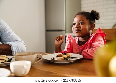 African american little girl smiling while having breakfast with family at home - Powered by Shutterstock