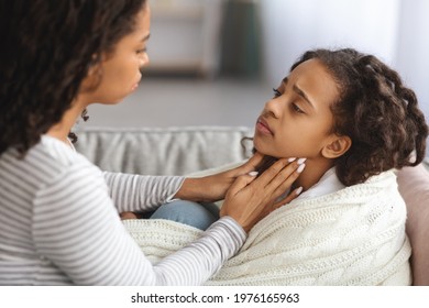 African American Little Girl Suffering From Sore Throat, Laying On Couch At Home, Closeup, Side View. Young Black Mother Taking Care Of Her Sick Daughter, Checking Her Glands, Touching Kid Neck