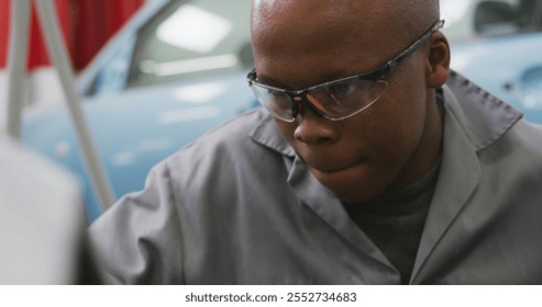 African American male car mechanic working in a township workshop, holding a screwdriver, using a hammer to repair a car - Powered by Shutterstock