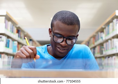 african american male college student sitting at desk in library and reading book. Reflections of paperwork on eyeglasses. Horizontal shape, front view