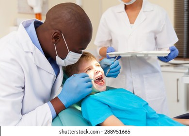 African American Male Dentist Examining Patient's Teeth In Dental Clinic