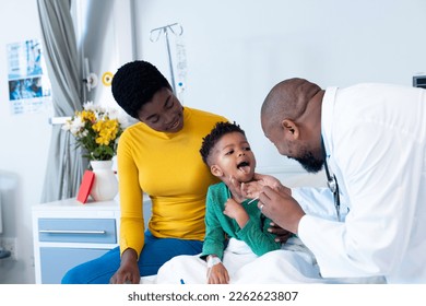 African american male doctor examining mouth of boy patient with mother in hospital. Hospital, medical and healthcare services. - Shutterstock ID 2262623807