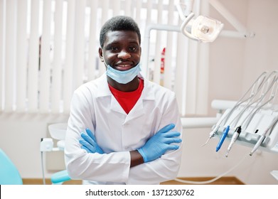 African American Male Doctor In Mask With Crossed Arms Sitting At Dentist Chair In Dental Clinic.