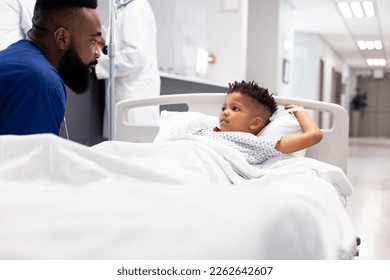 African american male doctor talking to boy patient in hospital bed in corridor with copy space. Hospital, medical and healthcare services. - Powered by Shutterstock