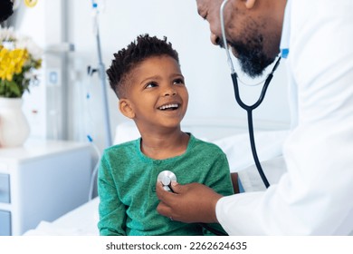 African american male doctor using stethoscope on smiling boy patient in hospital. Hospital, medical and healthcare services. - Shutterstock ID 2262624635