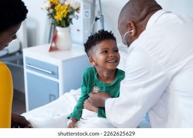 African american male doctor using stethoscope on smiling boy patient in hospital. Hospital, medical and healthcare services. - Shutterstock ID 2262625629