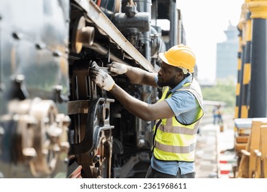 African American male engineer maintenance locomotive engine in locomotive repair garage. Male railway engineer use wrench repair train wheel in train garage