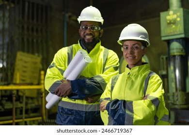 African American male and female engineers with blueprint working in heavy metal industrial factory. Confident two technician wearing vest and helmet safety standing at the manufacturing plant. - Powered by Shutterstock