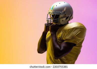 African american male american football player wearing helmet with neon yellow and purple lighting. Sport, movement, training and active lifestyle concept. - Powered by Shutterstock