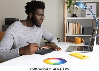 African American male graphic designer working at home using laptop and graphic tablet. Creativity and technology concept. - Powered by Shutterstock