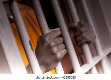An African American male with hands outside the bars of a prison cell