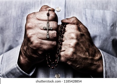 African American male hands praying holding a beads rosary with Jesus Christ in the cross or Crucifix on black background. Mature Afro American man with Christian Catholic religious faith