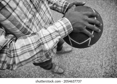 African American male holding a basketball while standing on pavement. 