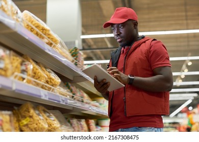 African American male manager of supermarket entering prices of food products into database while standing in front of shleves with cookies - Powered by Shutterstock