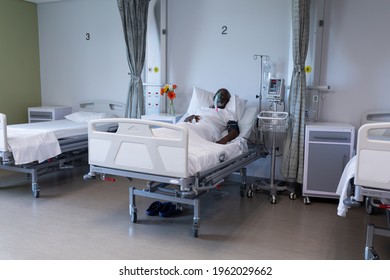 African American Male Patient Lying On Hospital Bed Wearing Oxygen Mask Ventilator. Medicine, Health And Healthcare Services During Coronavirus Covid 19 Pandemic.