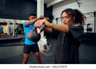 African American Male Personal Trainer Instructing African American Female With A Kettlebell Routine In The Gym. Mixed Race Friends Doing Cross Training Together. High Quality Photo