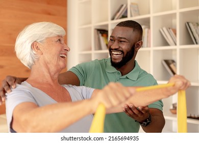 African American Male Physiotherapist Helping Senior Woman To Exercise With Resistance Bands. Medical Care And Retirement Senior Lifestyle Concept