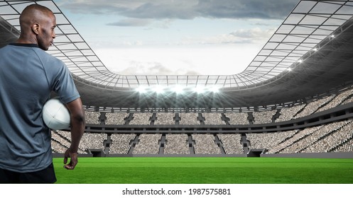 African american male rugby player holding a rugby ball against stadium in background. sports and fitness concept - Powered by Shutterstock