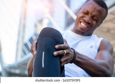 African American male runner bends over clutching his knee while in intense pain from an acute knee injury,Athletes hurt the knees.