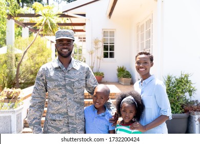 African American Male Solider Wearing Uniform And His Family Standing By Their House On A Sunny Day, Smiling And Looking Straight Into A Camera.