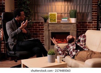 African American Male Therapist Consulting Man Laying On Couch, Doing Psychoanalysis To Solve Problems At Therapy Session. Talking About Behavior Issues And Giving Counseling Advice.