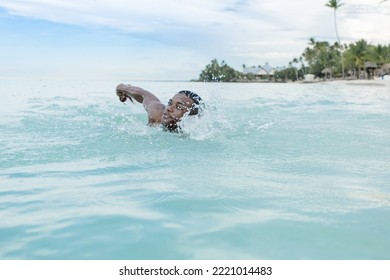 African American Male Traveler Swimming In Clean Sea Water Against Cloudy Blue Sky During Summer Vacation On Beach