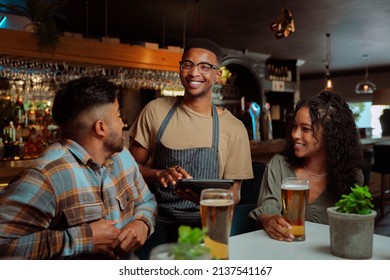 African American male waiter serving couple and friends at the restaurant - Powered by Shutterstock