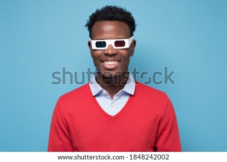 African american man in 3D glasses watching interesting movie on screen. Studio shot on blue wall.