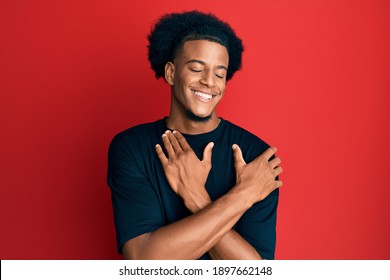 African american man with afro hair wearing casual clothes hugging oneself happy and positive, smiling confident. self love and self care 