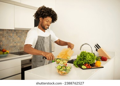 African American man in apron prepares vegetarian salad at modern kitchen table, showcasing healthy lifestyle and culinary hobby. Satisfaction of cooking nutritious meal - Powered by Shutterstock