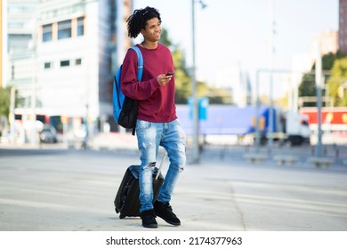 African American Man With Backpack And Mobile Phone Pulling Rolling Suitcase On City Street