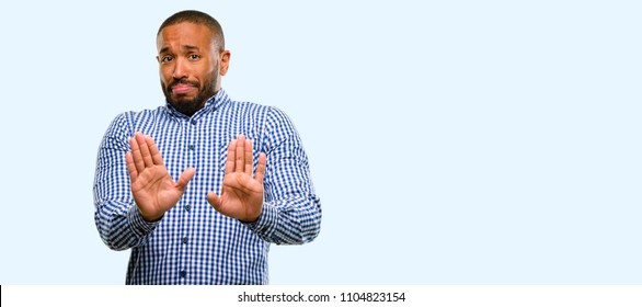 African american man with beard annoyed with bad attitude making stop sign with hand, saying no, expressing security, defense or restriction, maybe pushing isolated over blue background - Shutterstock ID 1104823154