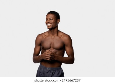 An African American man blissfully smiles, bare-chested with hands clasped together in a studio setting against a white backdrop. - Powered by Shutterstock